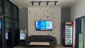 A modern lounge area with a sofa, a coffee table, a TV mounted on the wall, and a vending machine. - Aparthotel Greenhouse (Batumi)