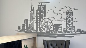 A room with a cityscape wall art, a green 'C' logo, and a tufted leather chair. - Aparthotel Greenhouse (Batumi)