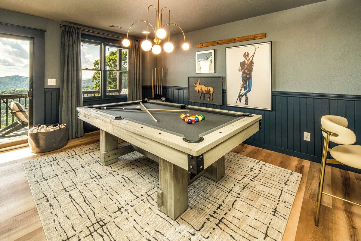 A pool table in a room with a view, a bar stool, and a framed picture on the wall.