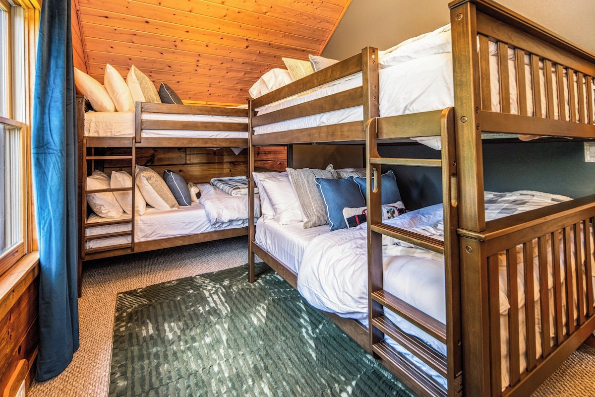 Una habitación con literas, una ventana con cortinas y techo de madera.
