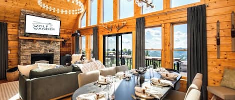 Un salon spacieux avec une cheminée, une grande table à manger dressée pour le repas et un coin salon confortable.