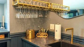 Un coin bar avec une étagère où sont rangés des verres à vin, un évier doté d’un robinet doré et un comptoir de bar agrémenté d’un objet décoratif.