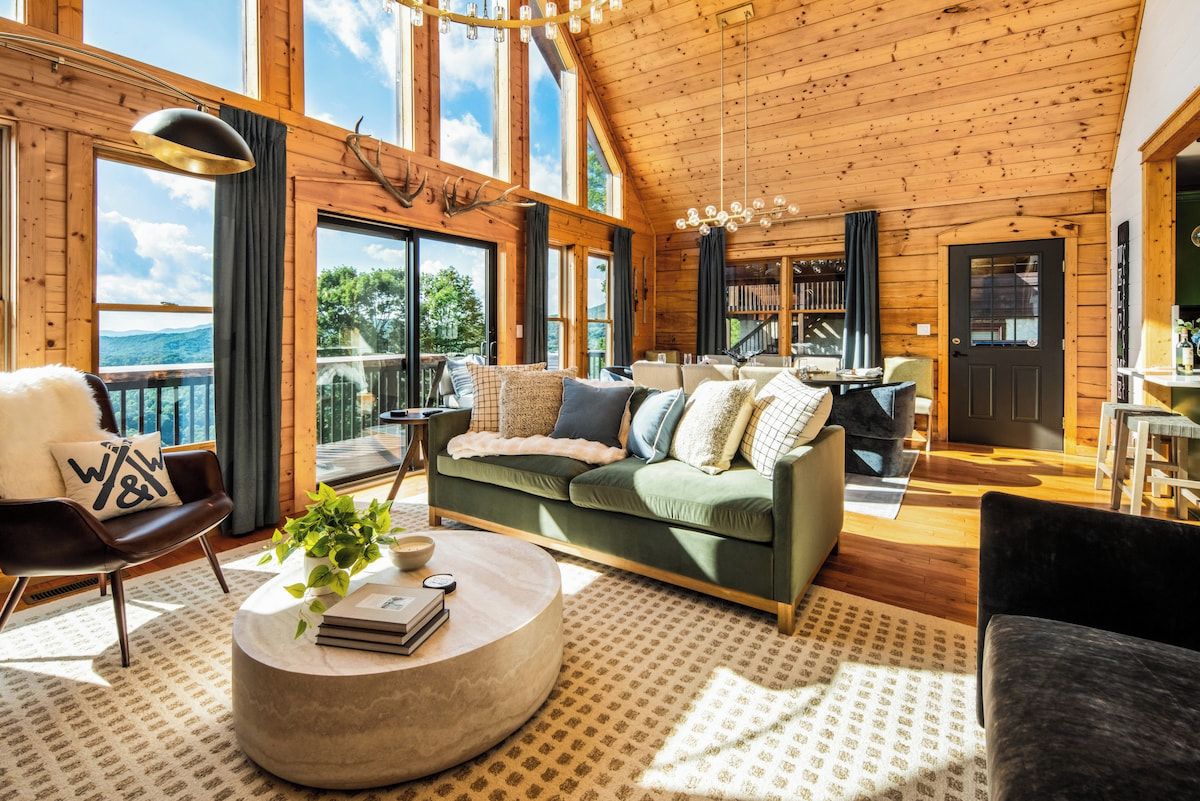 Interior acogedor de una cabaña con un sofá verde, una mesa de centro redonda y vistas al exterior a través de amplios ventanales.