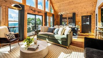 Interior acogedor de una cabaña con un sofá verde, una mesa de centro redonda y vistas al exterior a través de amplios ventanales.