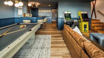 Ein Billardtisch mit Kugeln, eine Billardkeule, eine Couch und ein Neon-Leuchtschild in einem Raum mit Holzboden und blauen Wänden.