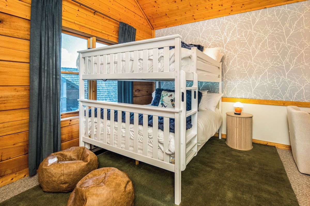 A bunk bed room with a view of the outside, a small bedside table, and two bean bags.