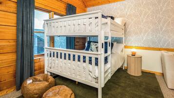 A bunk bed room with a view of the outside, a small bedside table, and two bean bags.