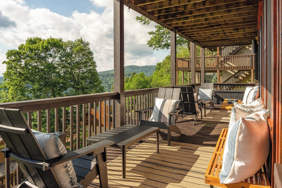 A wooden deck with outdoor furniture, including chairs and a bench, overlooking a forested area.