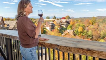Eine Person steht auf einer Holzterrasse und blickt auf ein Dorf mit Herbstlaub.