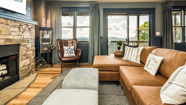 A cozy living room with a stone fireplace, a leather sofa, and a view of the outdoors. - 4,300ft Mountain Chalet - Sauna & Views (Mars Hill)