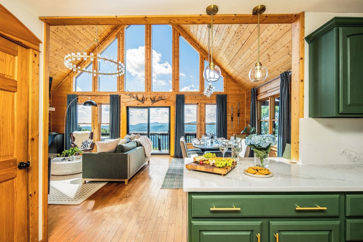 A spacious room with a high ceiling, wooden beams, a dining area with a table set for two, and a view of the outdoors.