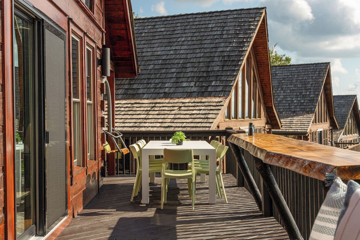Una terraza de madera con una mesa y sillas, con vista a una hilera de casas tradicionales con techos pronunciados.