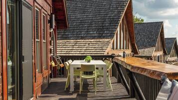 Una terraza de madera con una mesa y sillas, con vista a una hilera de casas tradicionales con techos pronunciados.