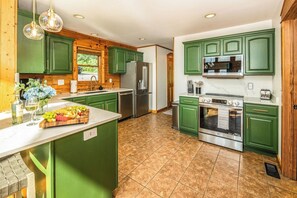 Una cocina con armarios verdes, un refrigerador de acero inoxidable, un horno empotrado y una isla grande con una bandeja de frutas.