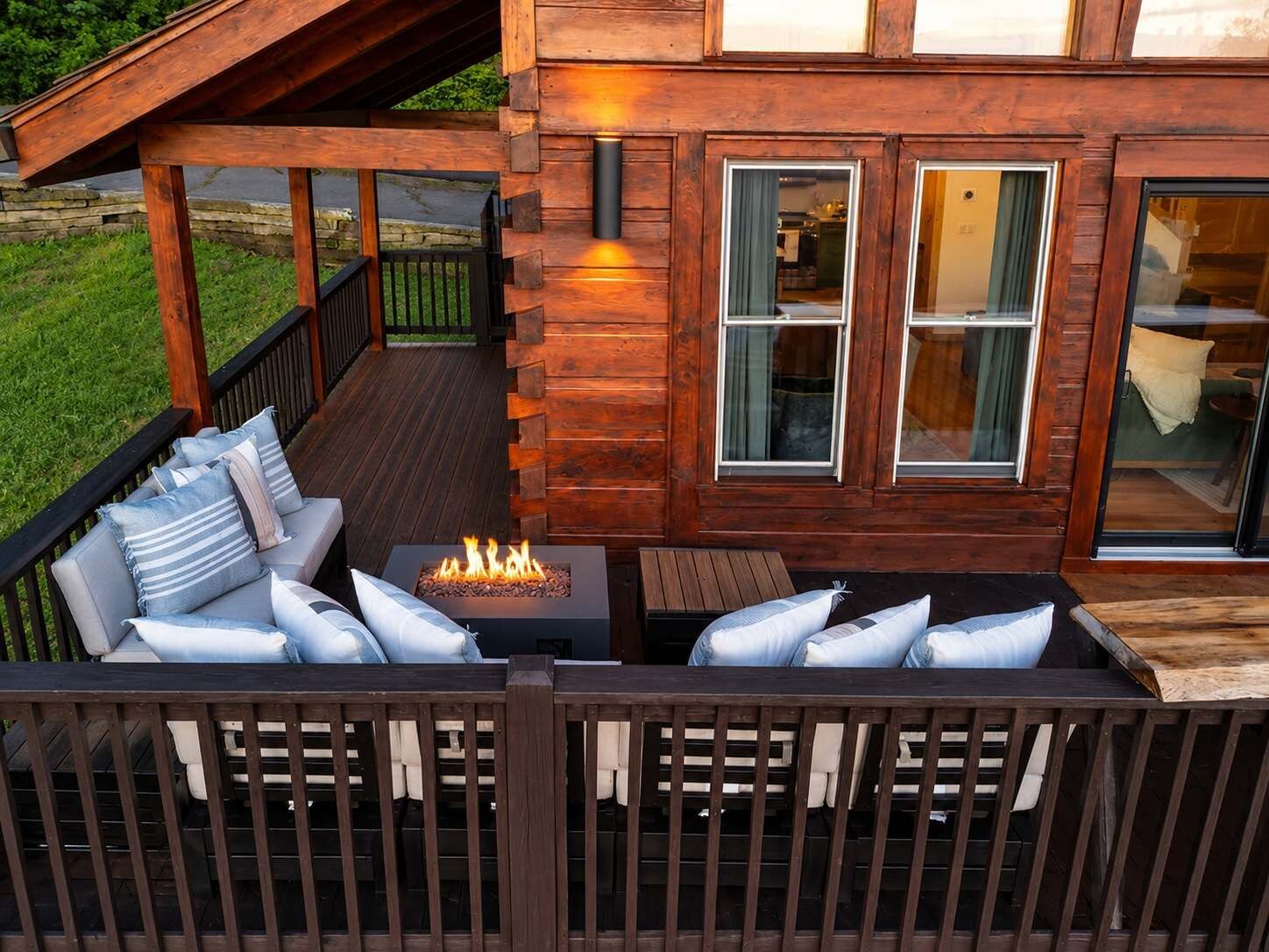 A wooden deck with a fire feature, outdoor seating, and a view of the interior.