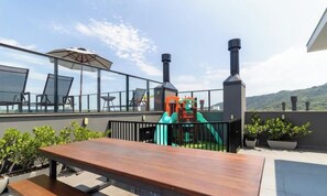 A rooftop terrace with a wooden table, chairs, a slide, and potted plants. - Building With Swimming Pool 800m From Beach - ACB (Florianópolis)