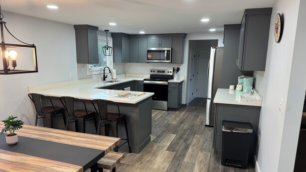 Une cuisine moderne avec des meubles gris, un îlot central, des appareils en acier inoxydable et un coin repas avec des meubles en bois.