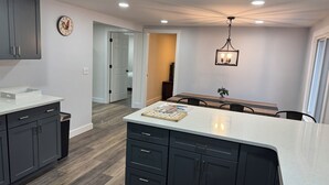 Une cuisine moderne avec des meubles de couleur sombre, un plan de travail blanc et un coin repas comprenant une table et des chaises.