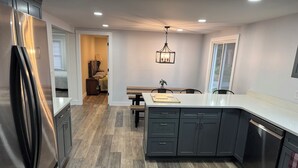 Une cuisine moderne avec un réfrigérateur en acier inoxydable, des meubles de rangement aux couleurs sombres et un plancher en bois.