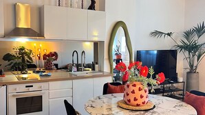 A modern kitchen with white cabinets, a stainless steel range hood, and a dining area with a marble table and black chairs.