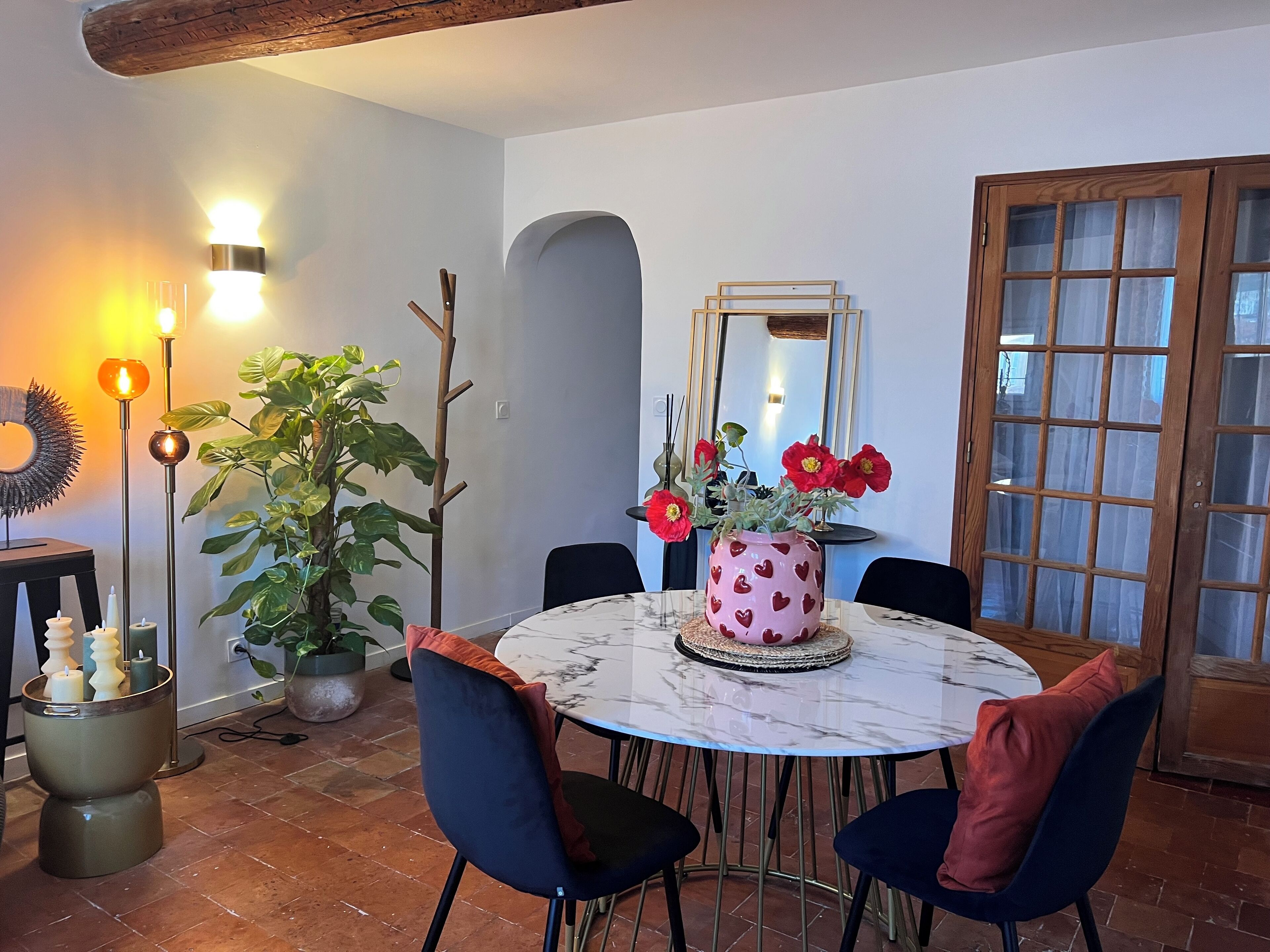 Een eetruimte met een marmeren tafel, vier stoelen, een potplant, een vaas met rode bloemen en een spiegel aan de muur.