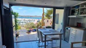 A modern kitchen with a dining area, a view of a marina, and a balcony with potted plants. - Facing the port, lovely studio on raised ground floor with large terrace, panoramic view (Bandol)