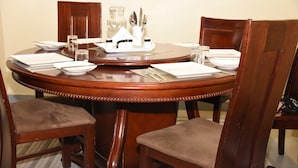 A round wooden dining table set with white plates, silverware, and a glass pitcher.