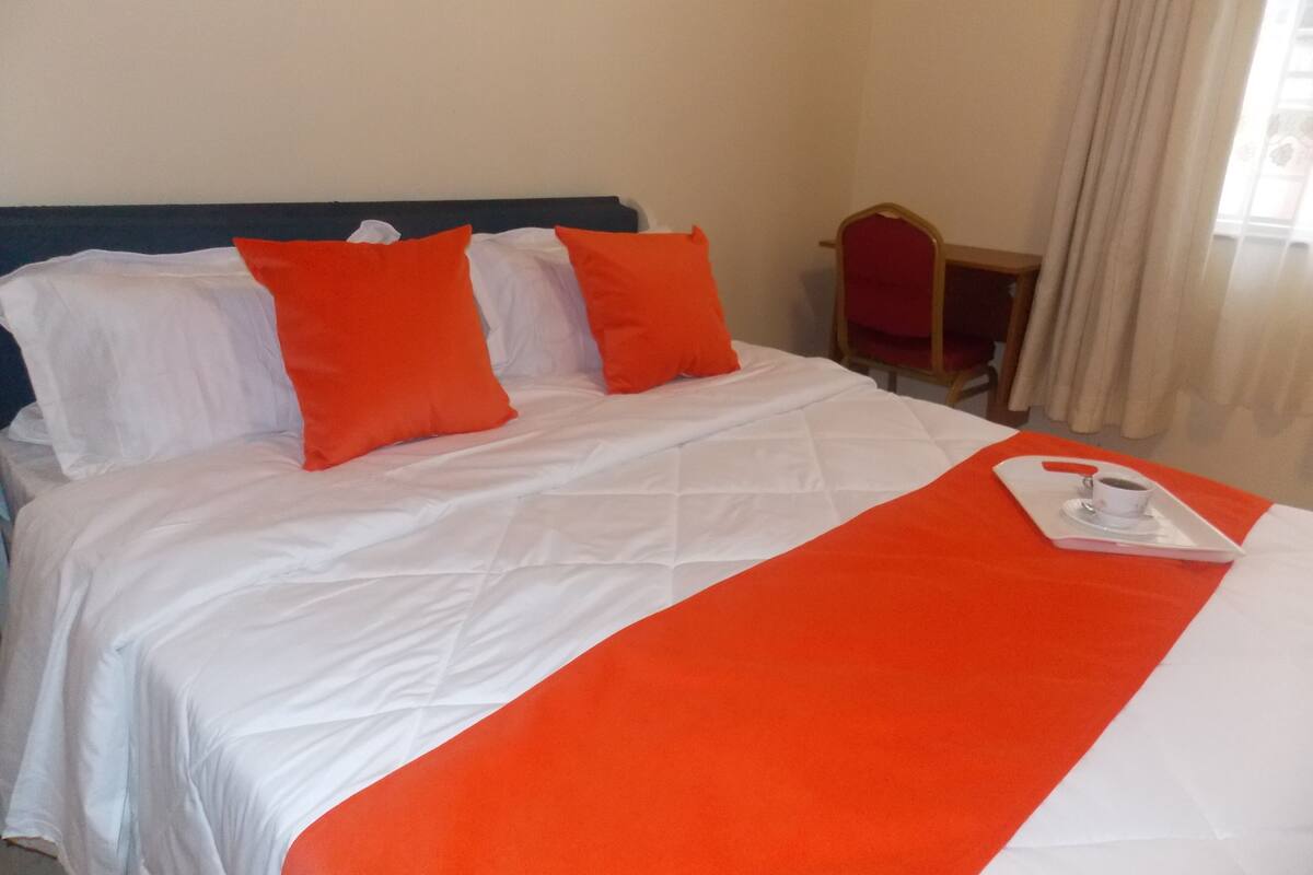 A hotel room with a bed, white bedding, and orange pillows.
