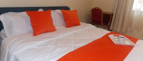 A hotel room with a bed, white bedding, and orange pillows.