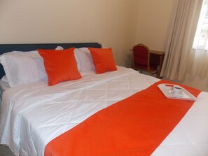 Una camera d'albergo con un letto, biancheria da letto bianca e cuscini arancioni.