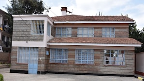 A two-story house with a tiled roof, multiple windows with blue frames, and a paved driveway.