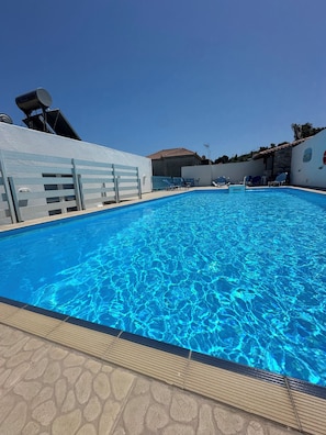 A swimming pool with clear blue water, surrounded by a stone deck and a white wall with a metal fence. - Galini Hellenic Hospitality (Alonissos)