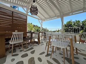 An outdoor patio with white and wooden furniture, a patterned floor, and a white pergola with a hanging light fixture. - Galini Hellenic Hospitality (Alonissos)