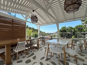 An outdoor patio with white tables and chairs, a wooden bench, and a patterned floor. - Galini Hellenic Hospitality (Alonissos)