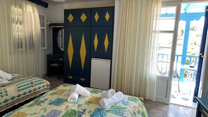 A hotel room with two beds, a ceiling fan, a small desk with a chair, a mirror, and a view of the outside. - Galini Hellenic Hospitality (Alonissos)