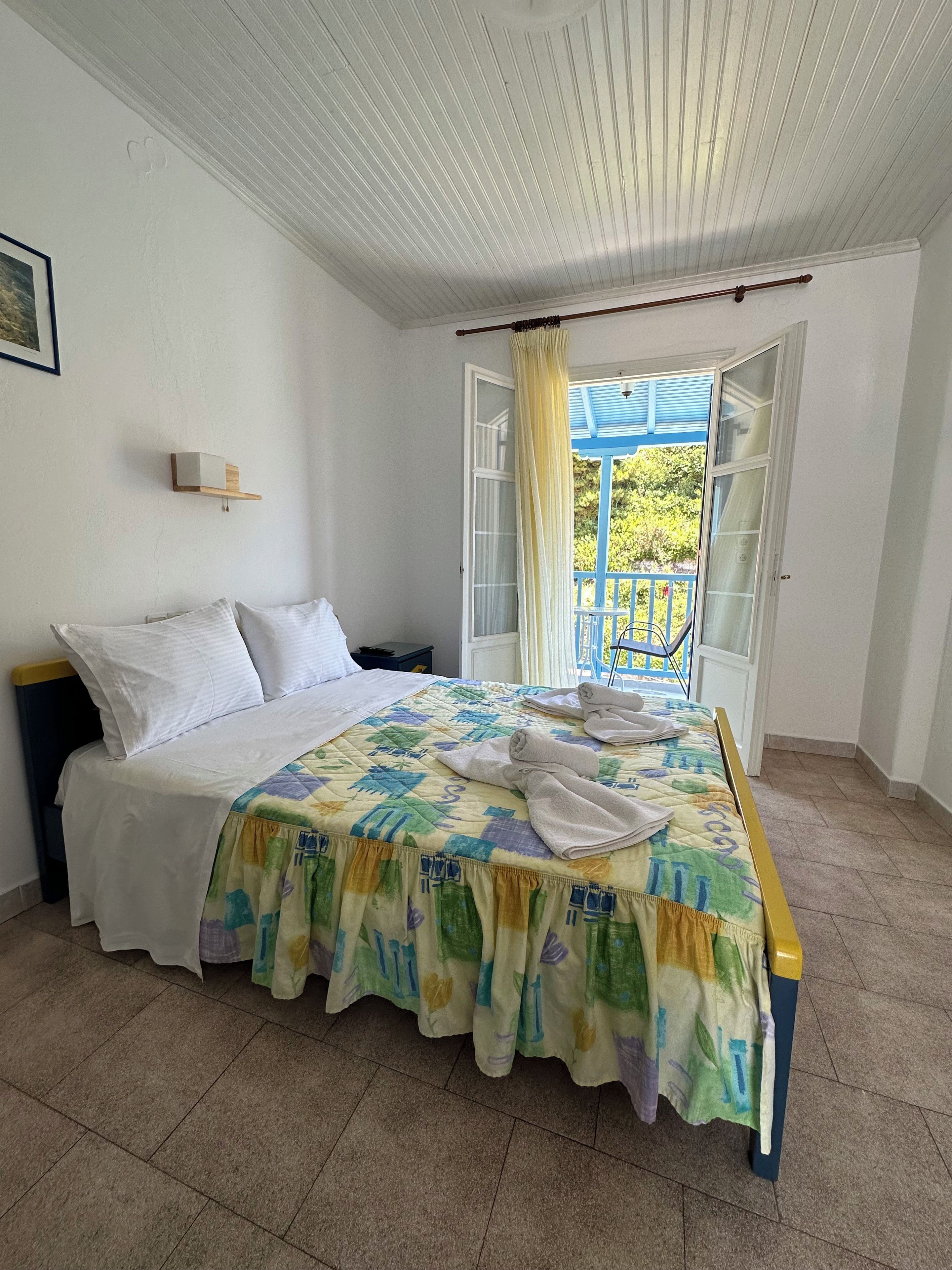 A bedroom with a bed, a nightstand, a window with curtains, and a view of the outside.