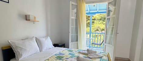 Un dormitorio con cama, mesita de noche, ventana con cortinas y vista al exterior.