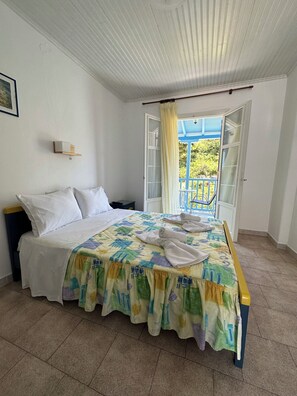 A bedroom with a bed, a nightstand, a window with curtains, and a view of the outside. - Galini Hellenic Hospitality (Alonissos)