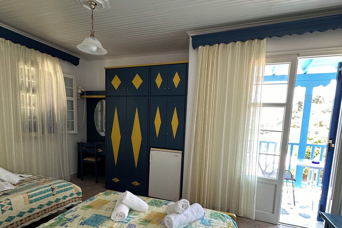 A hotel room with two beds, a ceiling fan, a small desk with a chair, a mirror, and a view of the outside.