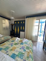 Habitación de hotel con dos camas, un ventilador de techo, un escritorio pequeño con una silla, un espejo y vistas al exterior.