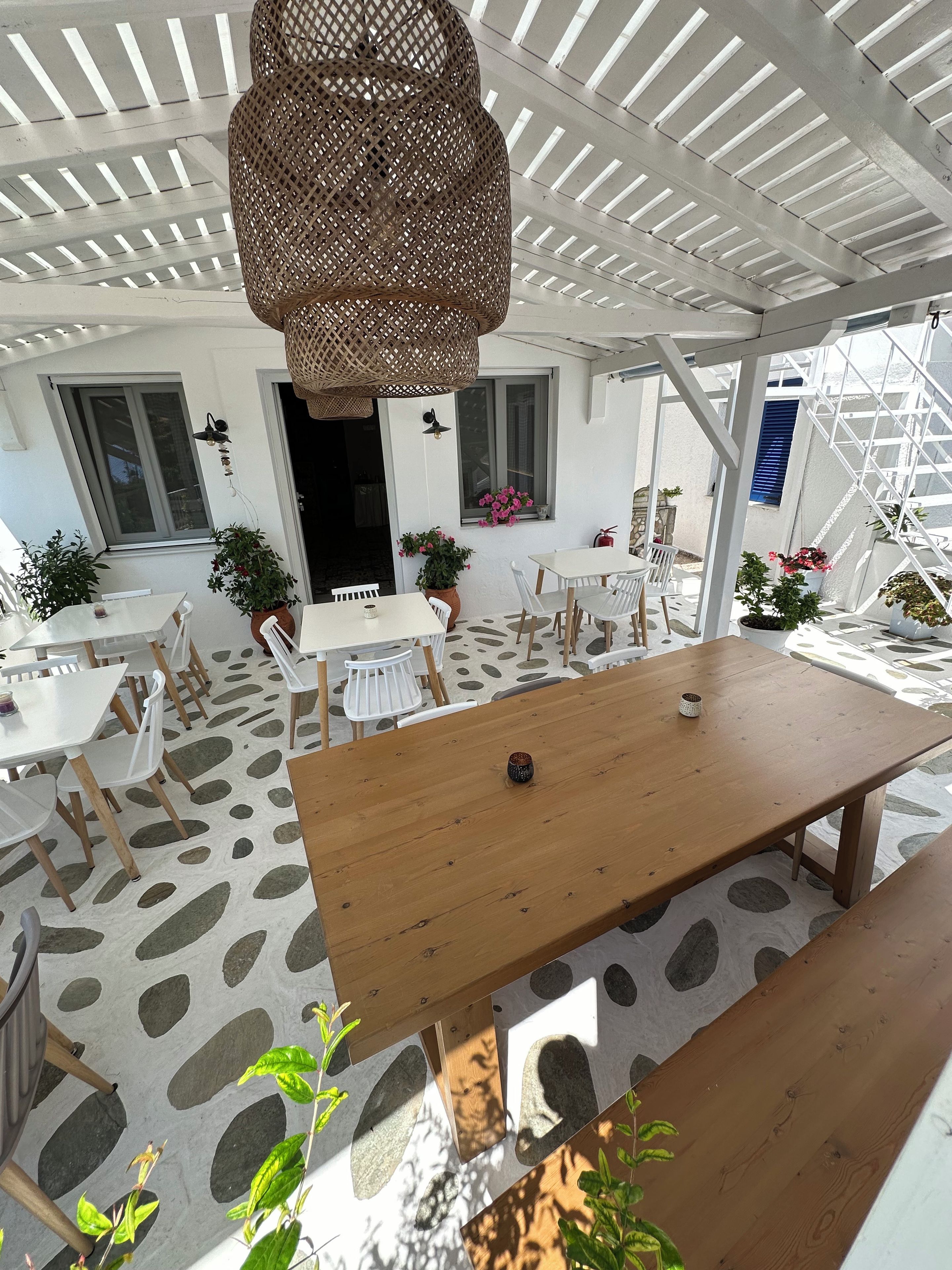 An outdoor patio with a wooden table and chairs, potted plants, and a hanging wicker lamp.
