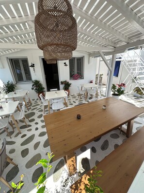 An outdoor patio with a wooden table and chairs, potted plants, and a hanging wicker lamp. - Galini Hellenic Hospitality (Alonissos)