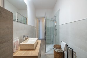 Ein modernes Badezimmer mit einem Holzwaschtisch, einer Duschkabine aus Glas und einem Korbwäschesessel.