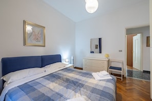 A bedroom with a bed, a dresser, a chair, and a door leading to another room.