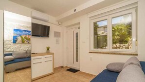 A compact room with a bed, a sofa, a small kitchenette, and a window with a view of palm trees. - Studio with air conditioning and barbecue facilities (Crikvenica)