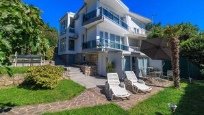A multi-story building with a balcony, stone steps, and a patio area with lounge chairs. - Studio with air conditioning and barbecue facilities (Crikvenica)