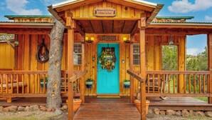 Eine Holzhütte mit einer türkisblauen Tür, einem Willkommensschild und einer Veranda mit Geländern.