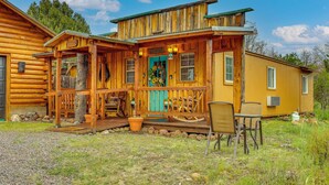 Une cabane en bois avec un porche, une porte bleue et un petit espace extérieur aménagé pour s’asseoir.