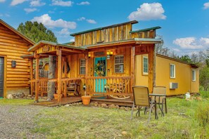 Une cabane en bois avec un porche, une porte bleue et un petit espace extérieur aménagé pour s’asseoir.