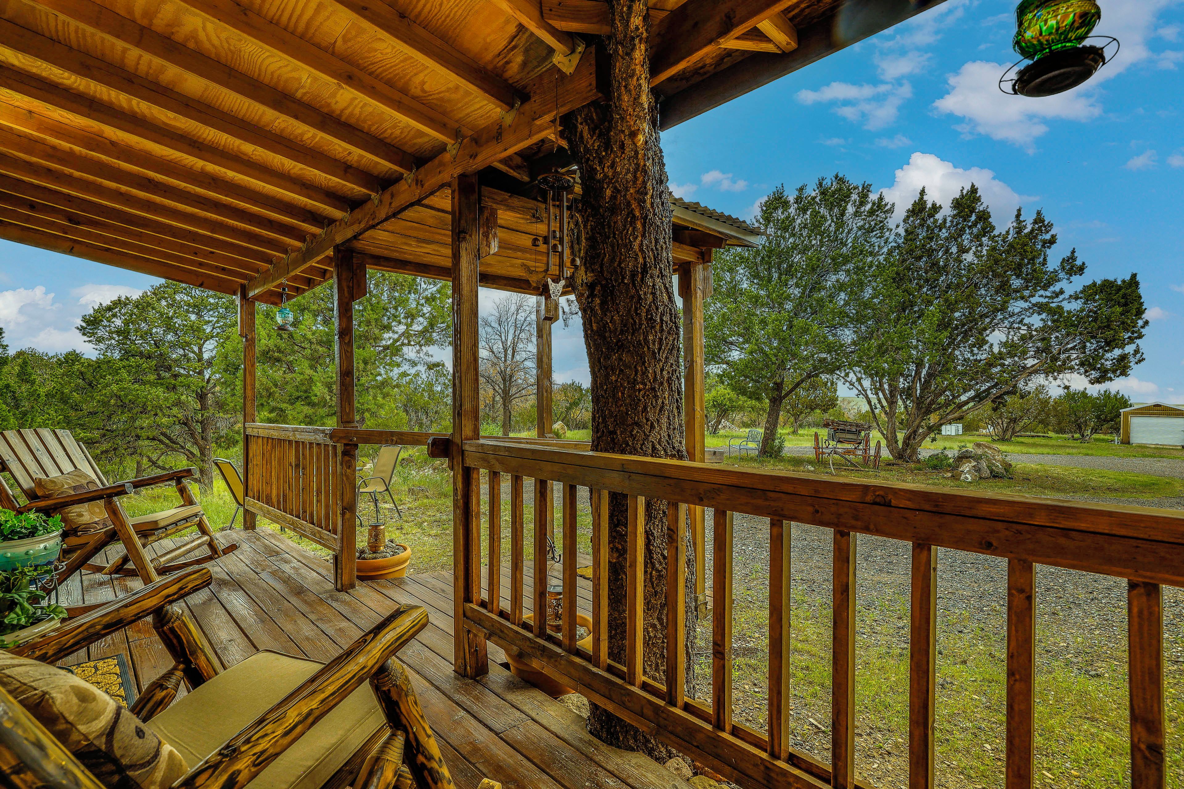 A wooden deck with a railing, chairs, and a tree trunk.